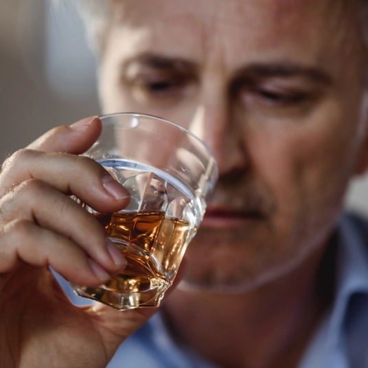 Signs a Person Is Drunk. An image of a man looking upset whilst holding a tumbler glass containing what appears to be whiskey.