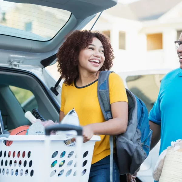 What is Empty Nest Syndrome? A slmiling father helping his daughter, who appears excited and is carrying a washing basket full of her personal items, relocate to university.